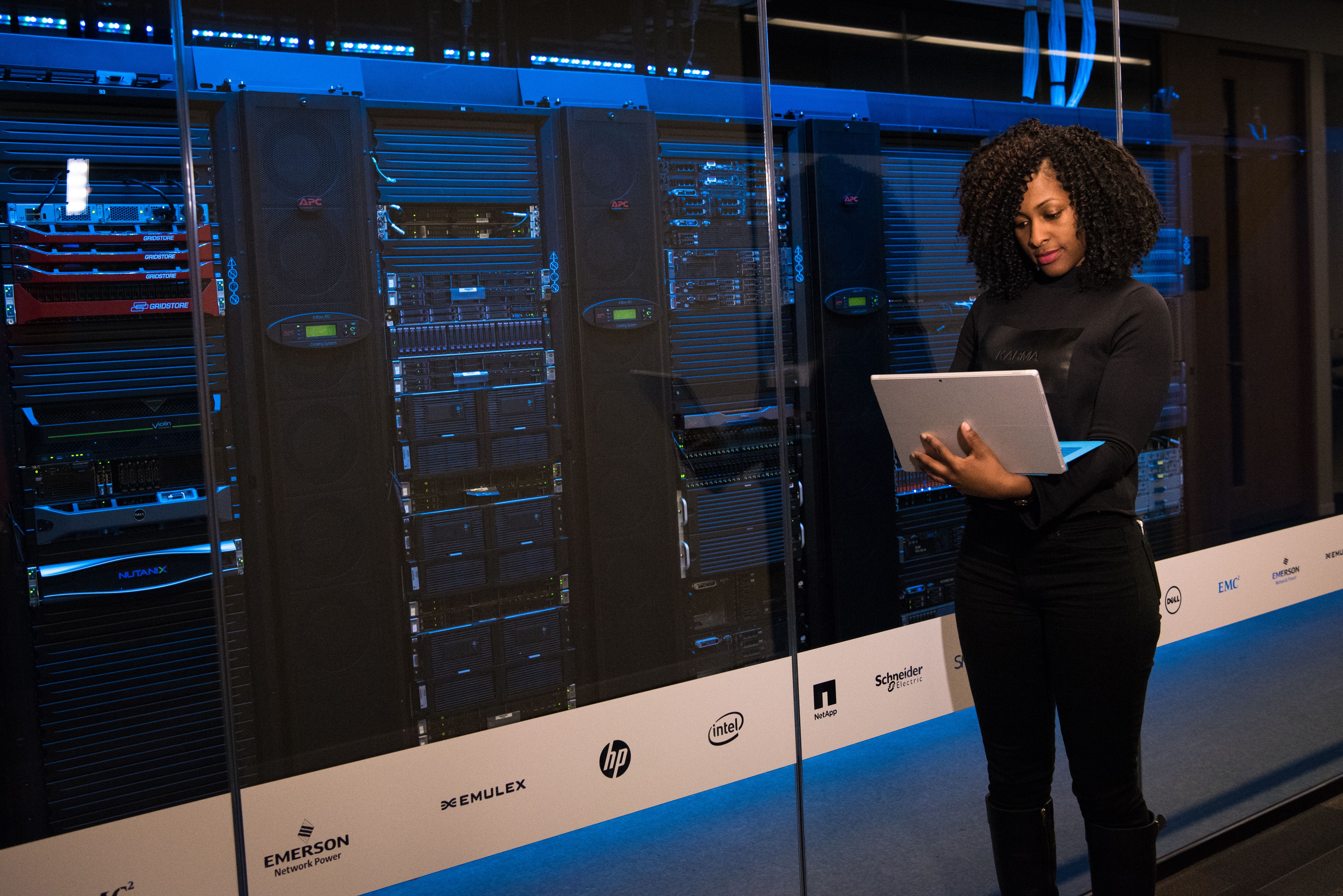 Cybersecurity engineer monitoring servers from a laptop in a modern data center.