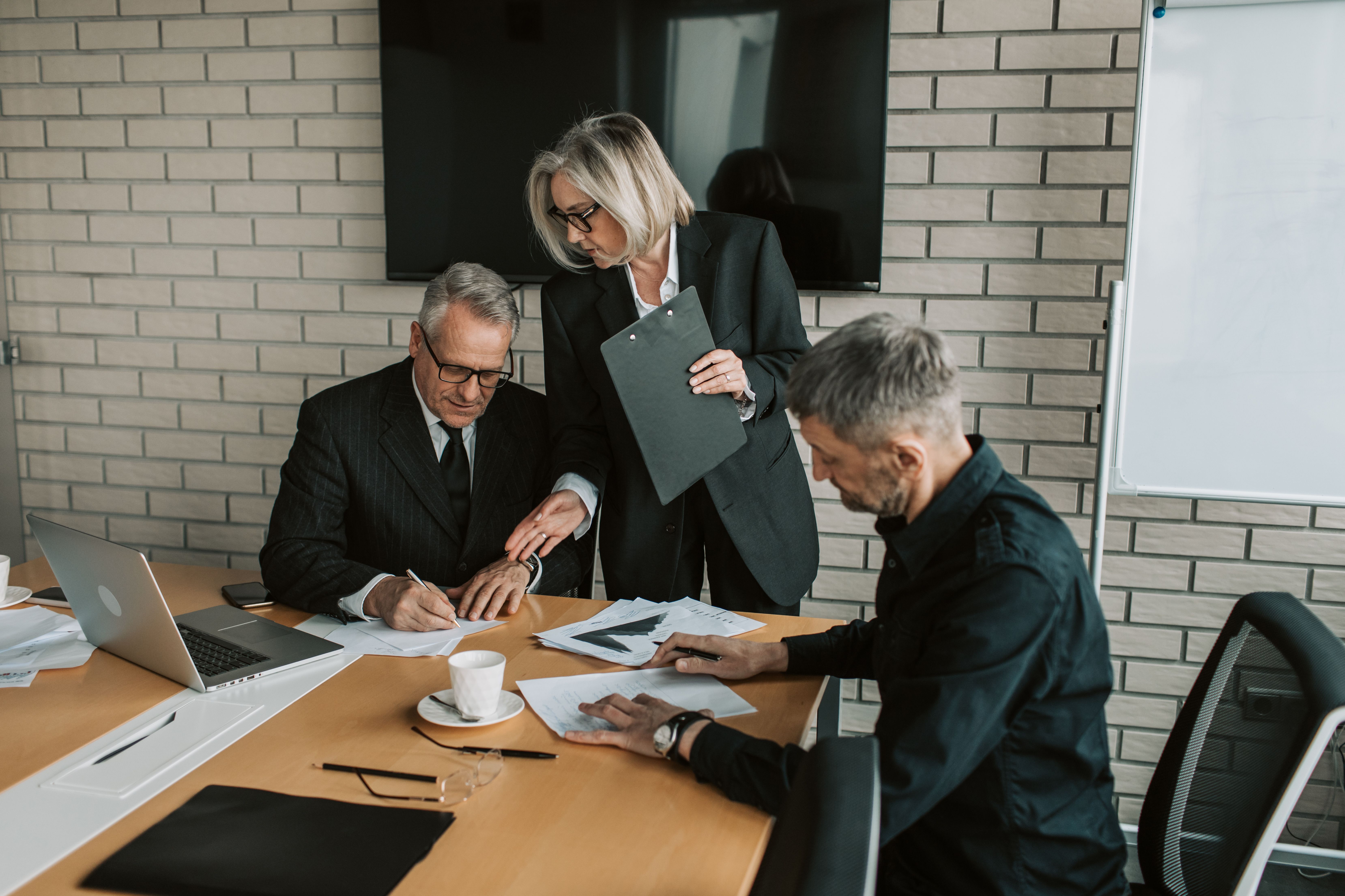 Senior professionals reviewing and signing documents at a business meeting, representing trust and discretion.